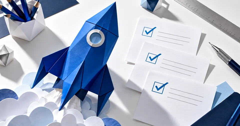 A blue paper rocket beside checked sheets representing website launch preparation.